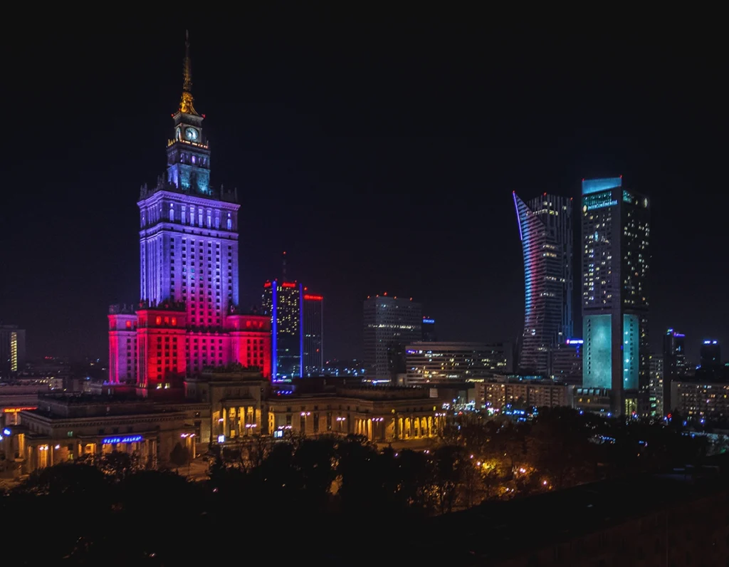 Stunning night view of Warsaw city center with illuminated skyscrapers and busy streets, capturing the vibrant atmosphere of the capital's nightlife.