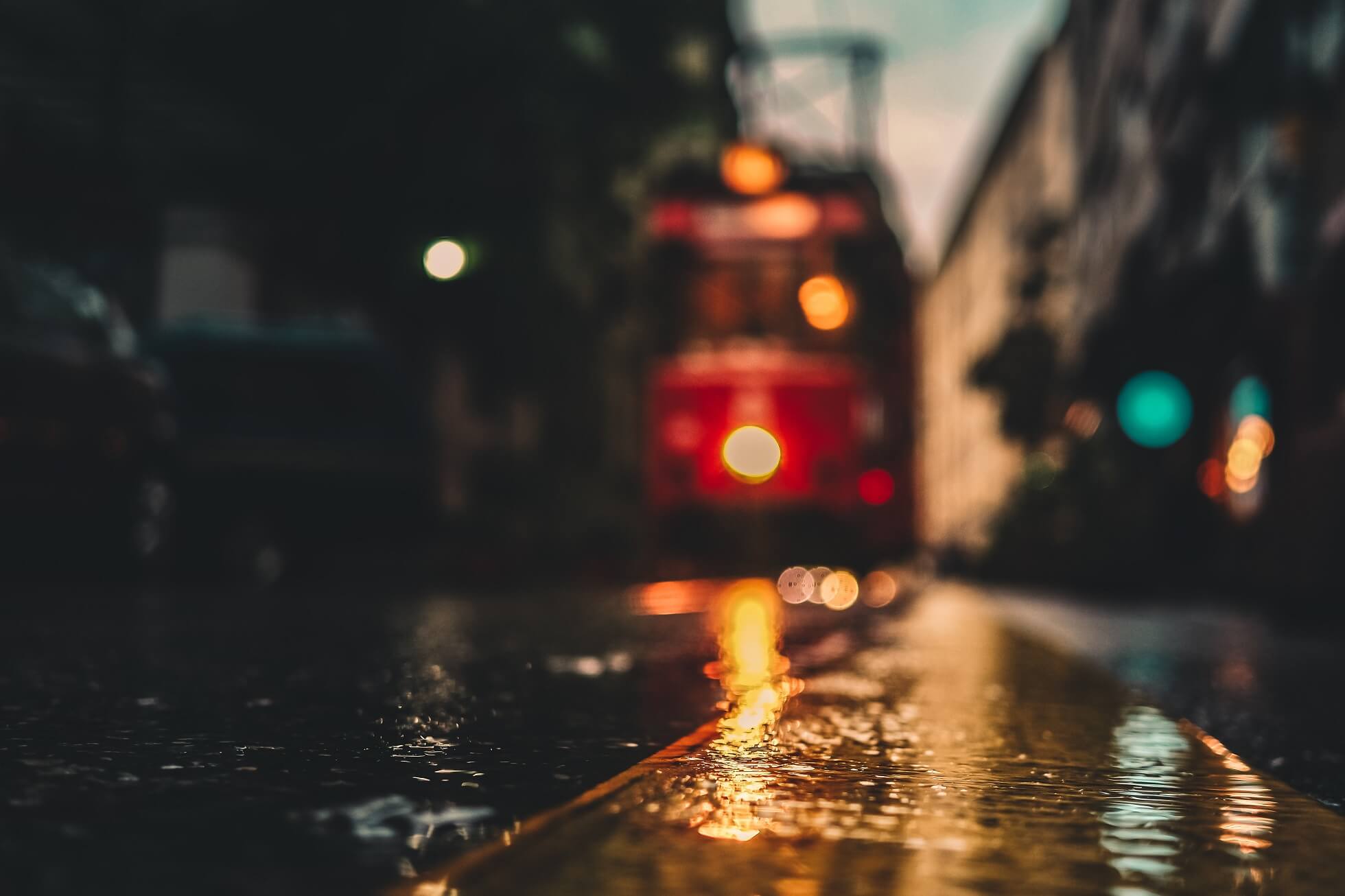 Close-up shot of a wet street in Warsaw at night, with the lights of a tram visible in the background, highlighting Warsaw's nightlife transportation.